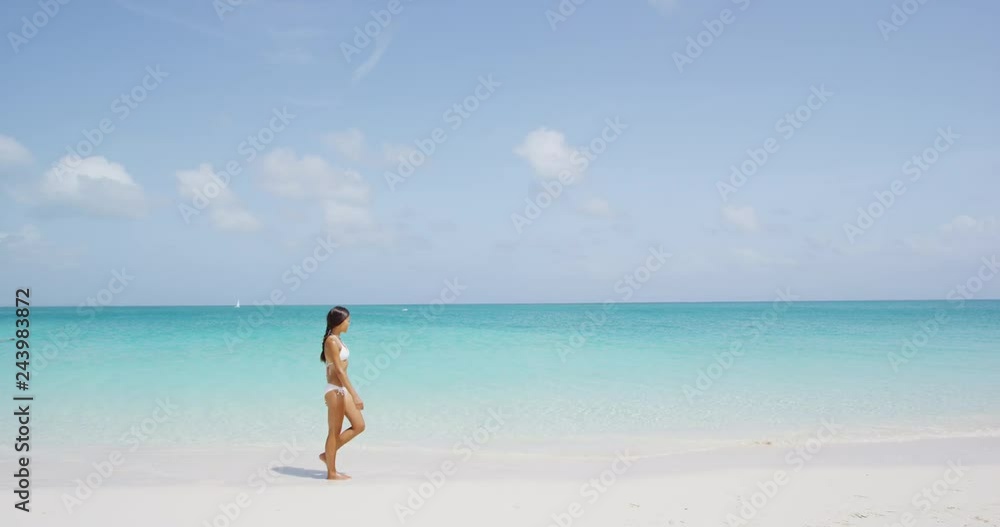 Beautiful woman in white bikini walking at beach. Young female is enjoying nature during her summer vacation. Scenic view of seascape against clear blue sky. Beautiful woman in white bikini walking at beach. Young female is enjoying nature during her summer vacation. Scenic view of seascape against clear blue sky.