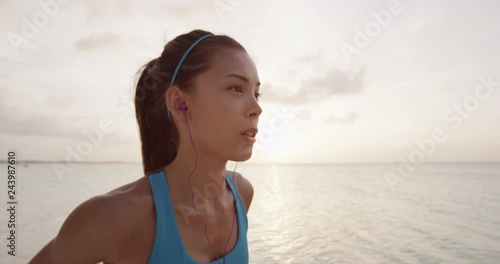 Runner woman getting ready to run and starts running on beach at sunset wearing earphones listening to music. STEADICAM SLOW MOTION, RED EPIC.