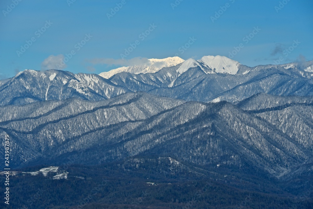 Panorama of snowy mountains. Winter forest and rocky peaks in the snow. Sunny winter day.