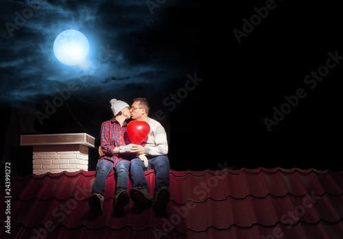 A married couple is sitting on the roof of a house at night.