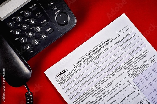 Tax Form 1040X and phone on a red velvet background, close-up photo