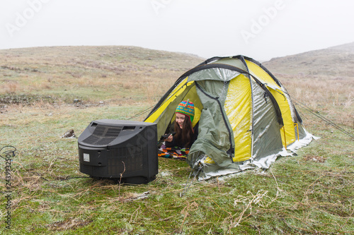 The girl on the nature lies in a tent and watches the old TV