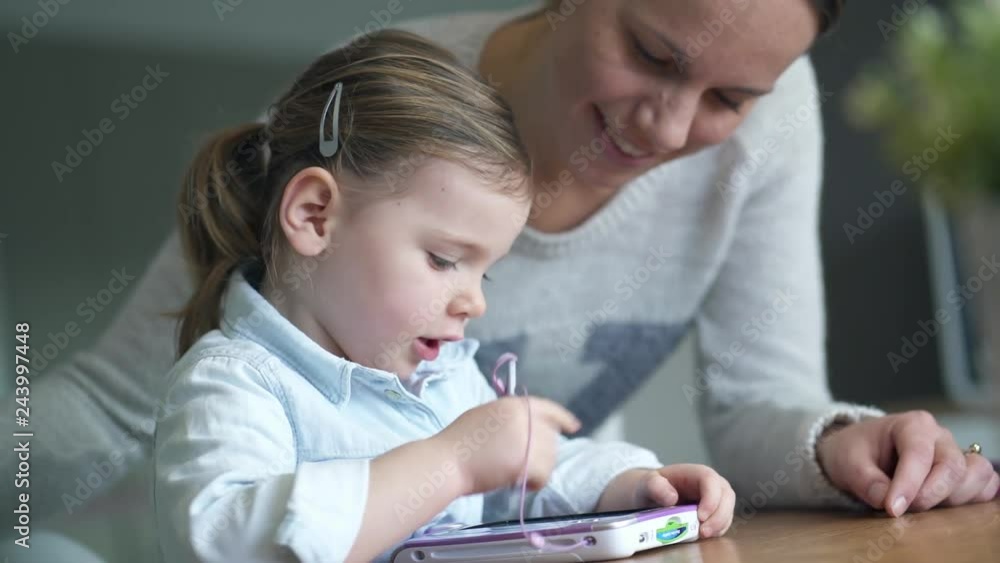 Mother and adorable young daughter playing games on kid's tablet at home Mother and adorable young daughter playing games on kid's tablet at home