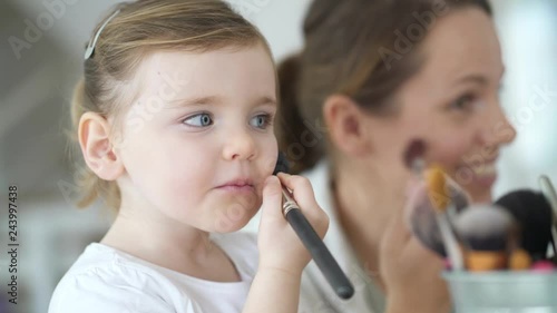 Adorable young daughter copying mother playing pretend with makeup brushes