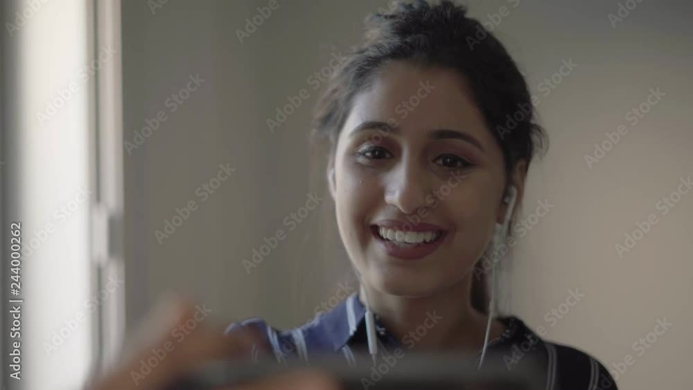 Laughing girl with earphones using smartphone for video call. Young woman talking to mobile phone screen, telling funny story or gossip. Video talk concept Laughing girl with earphones using smartphone for video call. Young woman talking to mobile phone screen, telling funny story or gossip. Video talk concept