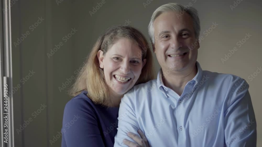 Portrait of happy mid adult family couple. Middle aged man and woman smiling at camera, lady hugging her husband, he keeping arms crossed. Happy union concept Portrait of happy mid adult family couple. Middle aged man and woman smiling at camera, lady hugging her husband, he keeping arms crossed. Happy union concept