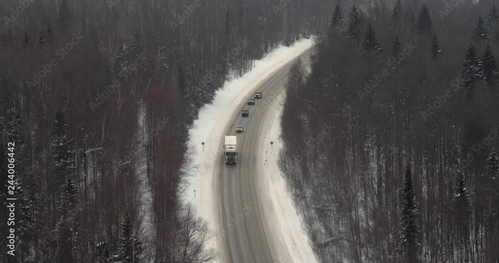 One dirty truck with white trailer driving on a dirt highway in mountains in winter cloudy day - Aerial drone view One dirty truck with white trailer driving on a dirt highway in mountains in winter cloudy day - Aerial drone view