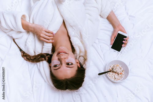 Foto happy young girl woke up early, lying on a bed in a white terry dressing gown, u
