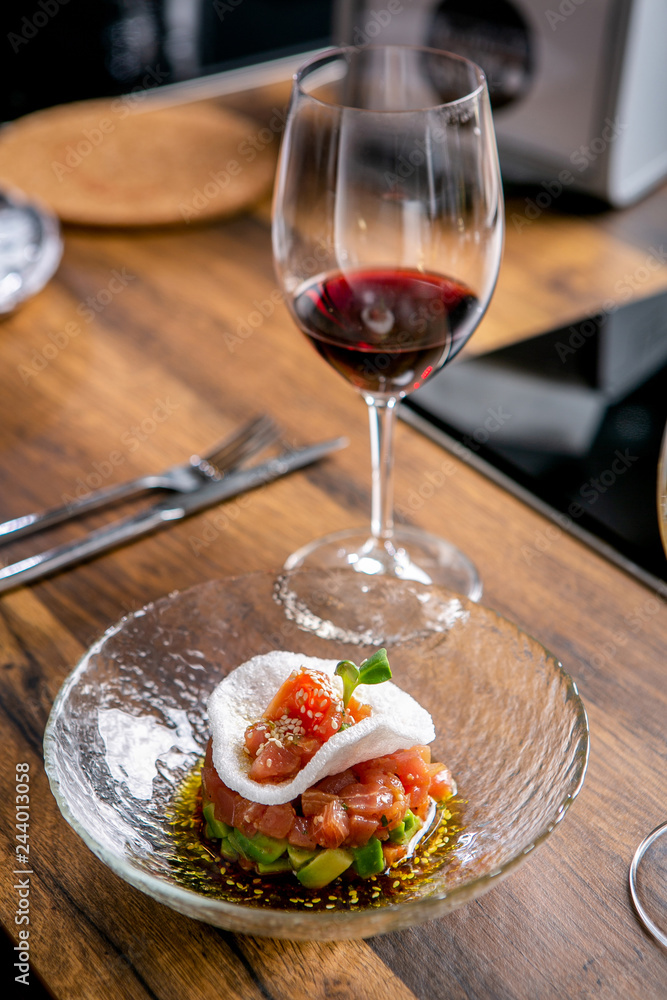The layout of the finished dish. Tuna tartar on a plate and a glass of red wine. Master class in the kitchen. The process of cooking. Step by step. Tutorial. Close-up