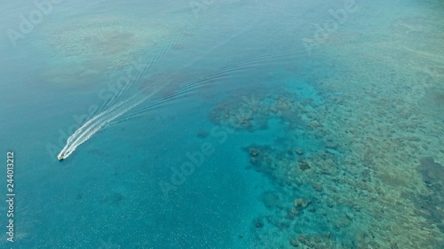stunning aerial drone image of a a small fishing boat entering an a sea ocean anchorage in a channel next to a coral reef in crystal clear azure blue water at a remote isolated tropical island