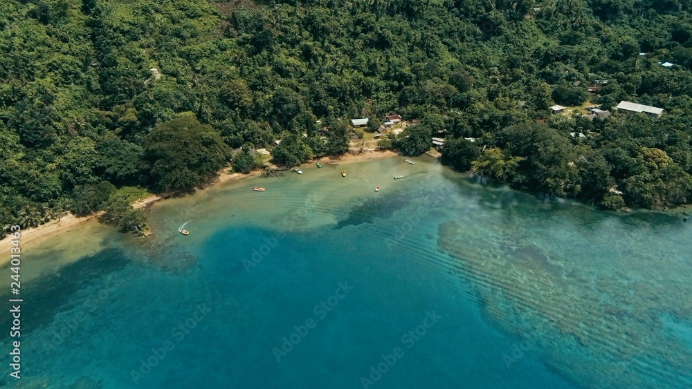 aerial drone image of a south pacific village on a remote island with a beautiful coral reef and lush tropical rainforest jungle while a small motor boat approaching aerial drone image of a south pacific village on a remote island with a beautiful coral reef and lush tropical rainforest jungle while a small motor boat approaching