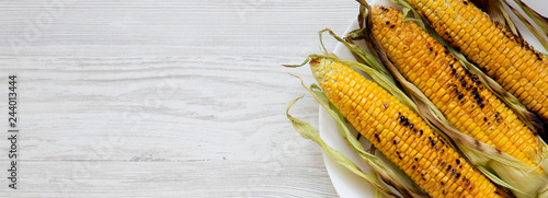 Photography Grilled corn on the cob on a white plate over white wooden background, top view