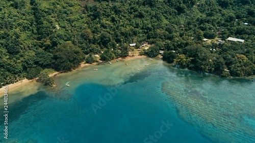 aerial drone image of a south pacific village on a remote island with a beautiful coral reef and lush tropical rainforest jungle while a small motor boat approaching