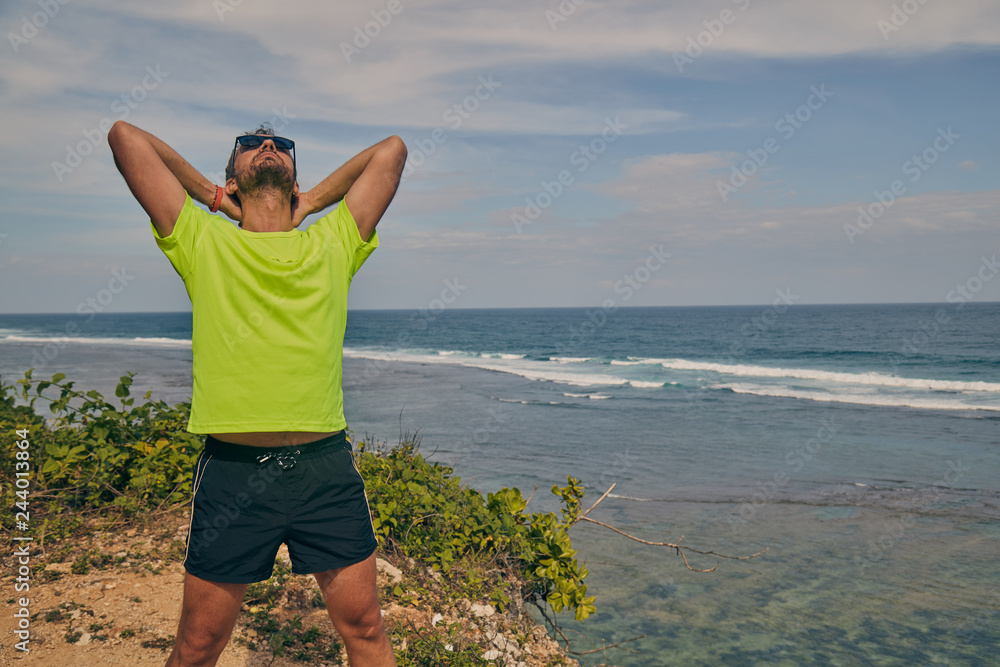 Sportsman stretching on a tropical exotic cliff near the ocean.