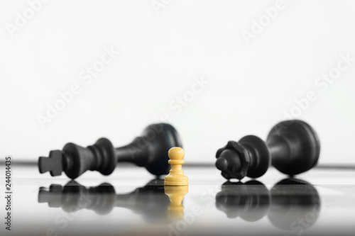 фотографія White peon standing victorious in front of a defeated King and Queen black chess