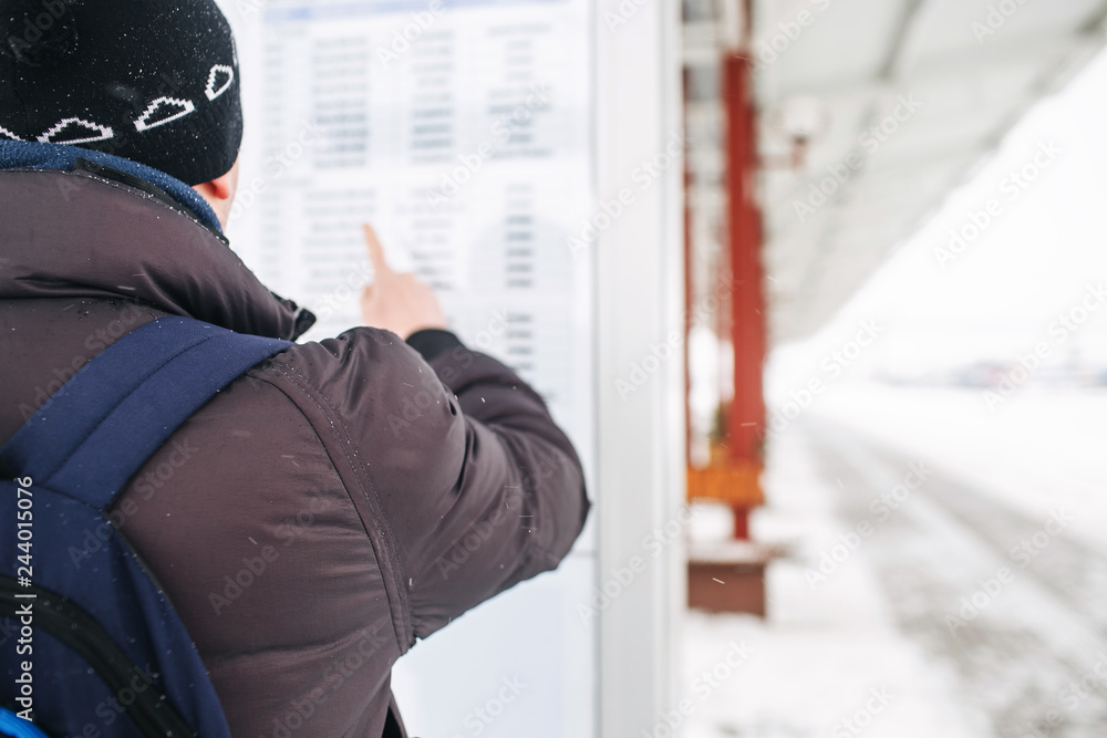 man traveler studies standing on the railway platform and studying the train schedule in winter