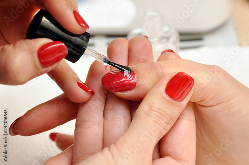 A manicurist paints a customer s nails. Painting nails with red lacquer close-up.