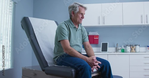 Senior Caucasian male patient waiting for doctor sitting on exam room table