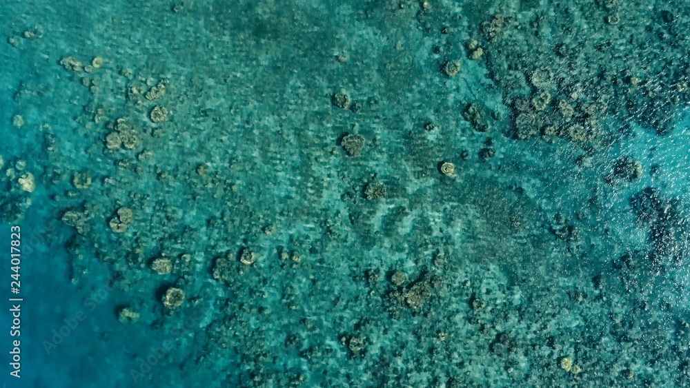 stunning aerial drone image of a a small fishing boat entering an a sea ocean anchorage in a channel next to a coral reef in crystal clear azure blue water at a remote isolated tropical island