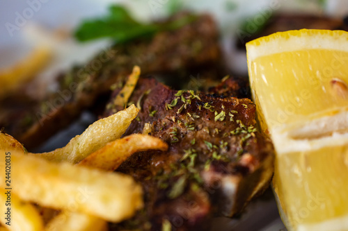 Delicious Serving Of Grilled Large T-Bone Steak Seasoned With Herbs By French Fries And Lemon Slice