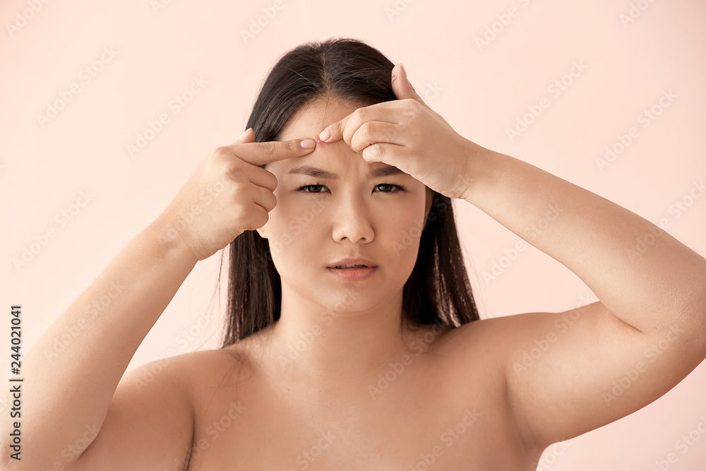 Portrait of young Asian woman with acne problem squishing pimples on color background Portrait of young Asian woman with acne problem squishing pimples on color background
