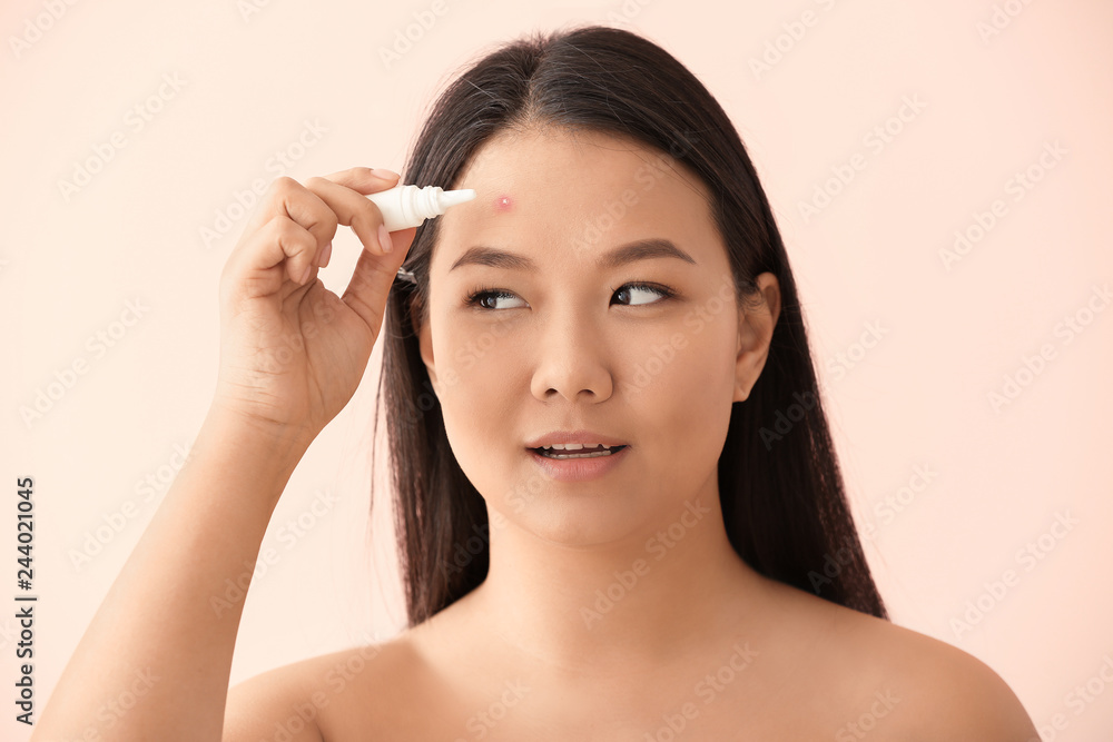 Portrait of young Asian woman with remedy for acne on color background