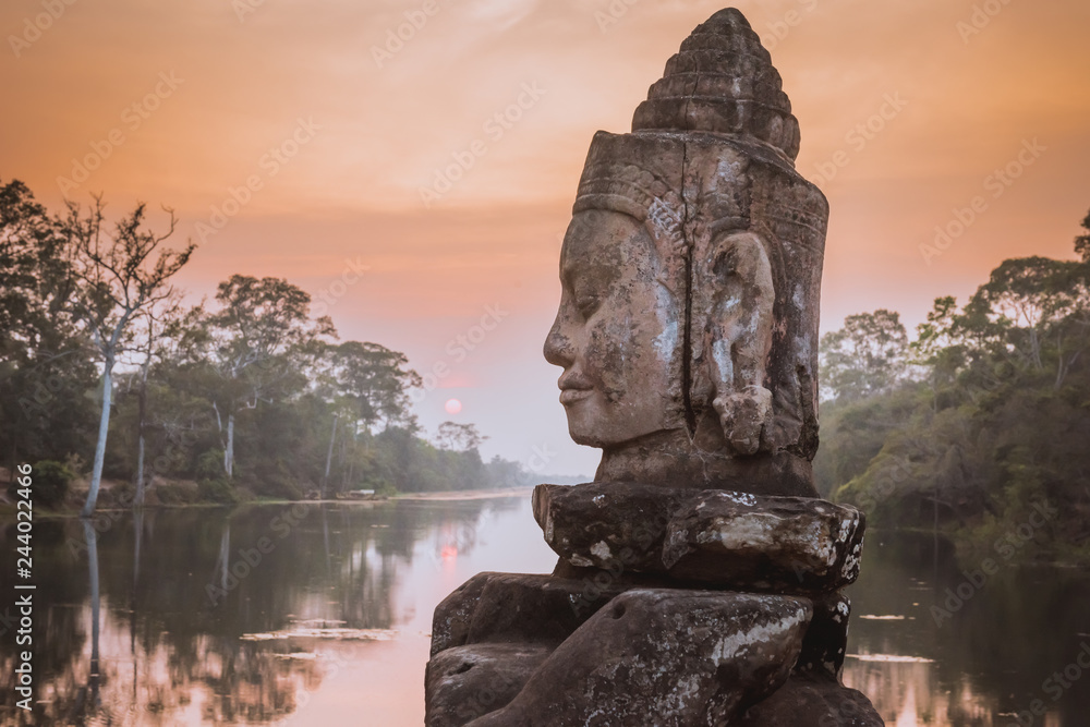 Fototapeta premium Kamienny Asura na grobli blisko Południowej bramy Angkor Thom w Siem Przeprowadza żniwa, Kambodża. Piękny zmierzch nad antyczną fosą w tle. Angkor Thom jest popularną atrakcją turystyczną.