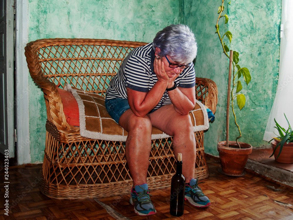 Φωτογραφία A drunk senior woman with a wine bottle in her hand sitting in a sofa