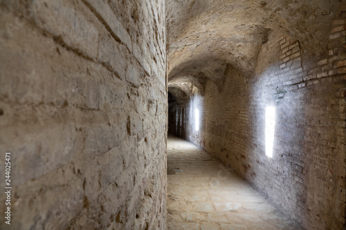 Curved stone tunnel with sun light beams and dark end