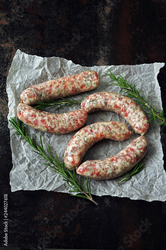 Raw sausages with rosemary for grilling or barbecue. Appetizing Munich sausages in paper. Top view.
