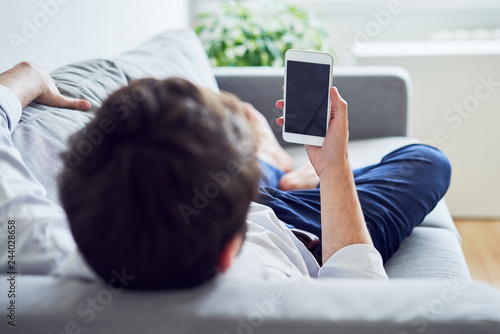 Young man using smartphone while lying on sofa