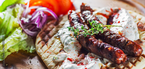 grilled meat sausages with pita bread and vegetables salad and tzatziki dip on wooden board photo