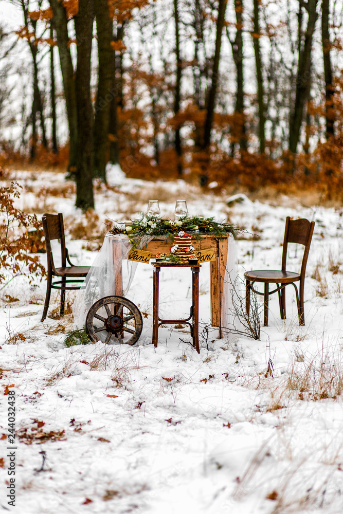 Wedding old wooden table with needlepoint and leaf decoration during wedding ceremony in winter on snow in the middle of forest covered with fresh snow