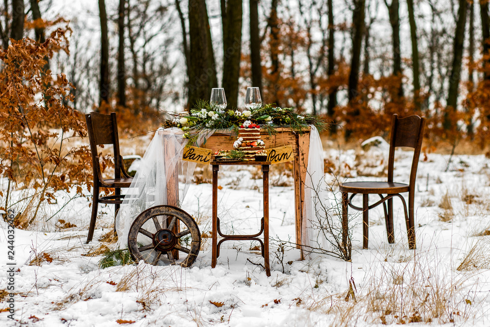 Wedding old wooden table with needlepoint and leaf decoration during wedding ceremony in winter on snow in the middle of forest covered with fresh snow