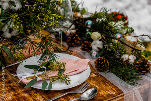 Wedding old wooden table with decoration full of flowers and placement prepared for food during the wedding ceremony in winter on snow in the middle of forest covered with fresh snow