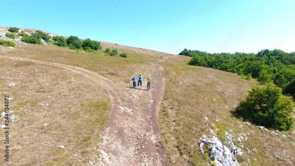 Aerial: Three tourists stand on the road in mountains and look through binoculars of mountain summer Crimea. Dynamic bright scene with people movement. Youth active lifestyle location.