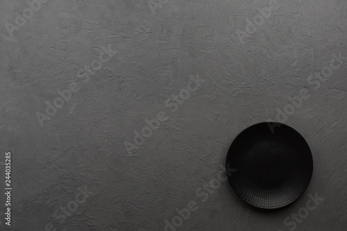Black plate on dark stone background. Copy space, top view.