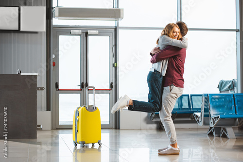 attractive woman hugging boyfriend in waiting hall near suitcase