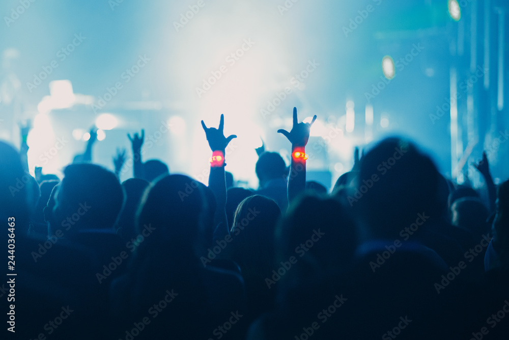Concert, event or party concept. People with hands up near the scene, spotlight, colored blue light.