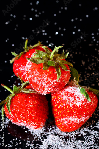 Ripe organic strawberries with granulated sugar on black glass