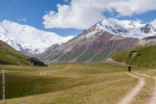 Man standing on tire tracks in a valley surrounded by snow capped mountains, Tulpar Kul, Kyrgyzstan, looking towards Peak Lenin. photo