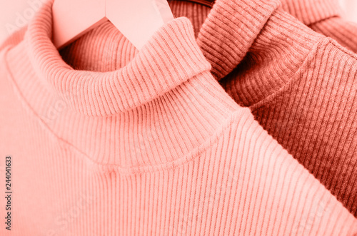 Warm sweaters hang on a coral-colored coat hanger.