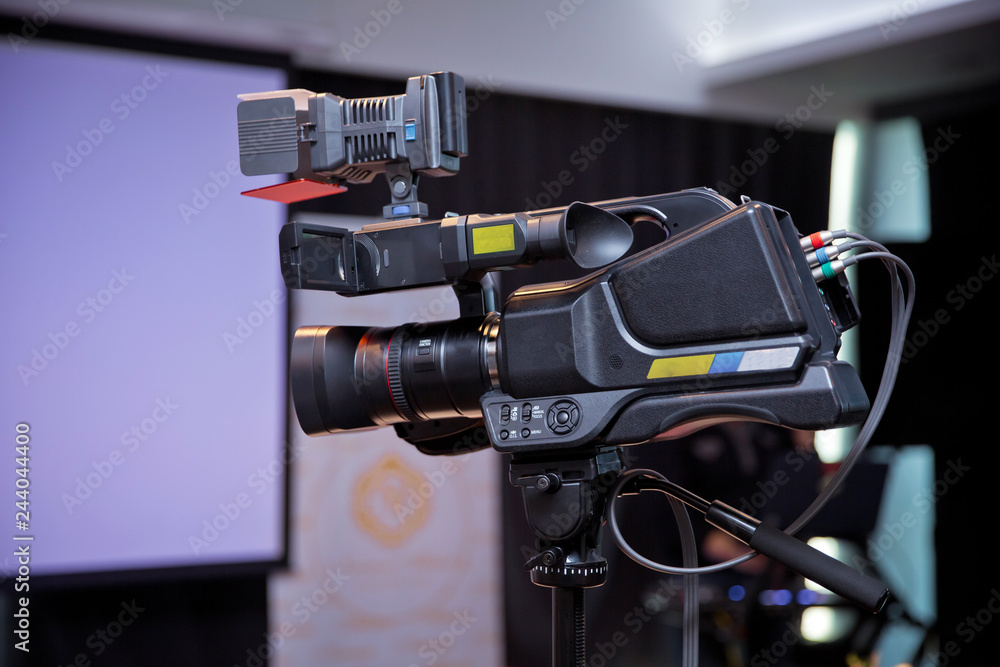 Fototapeta premium Professional digital camera with microphone on the tripod recording video .Camera recording publicity event . Press conference. Filming an event with a video camera. on the tripod in the room - Image