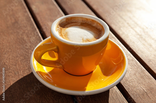 cappuccino in a yellow cup on a wooden table