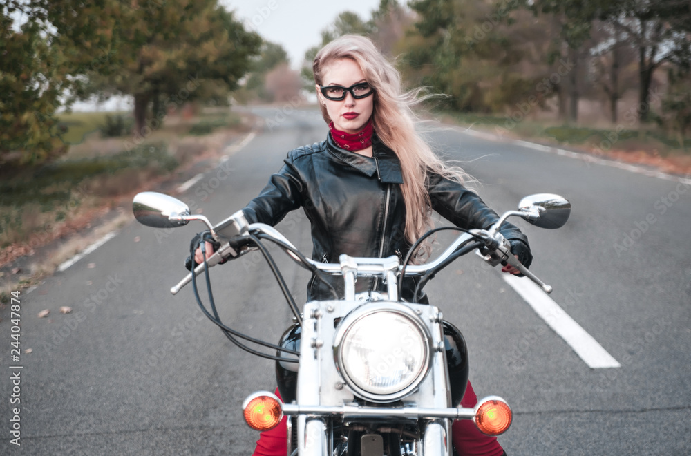 Beautiful biker woman posing outdoor with motorcycle on the road.

