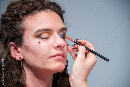 Close-up of a girl's face while being put on make-up by a professional make-up artist. Eye theme on makeup artist. Beauty, fashion and conceptual detail still life. Uniform white background.
