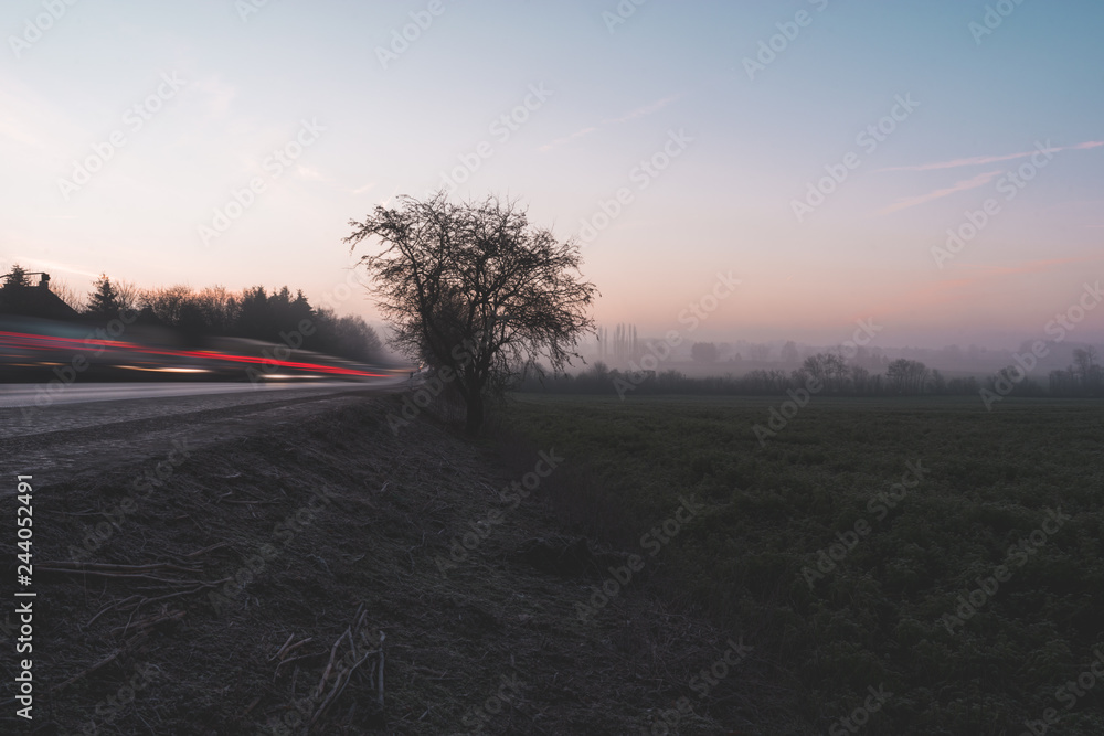 Light trails and field against the sunrise colored background
