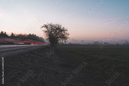 Light trails and field against the sunrise colored background