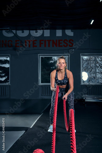 Vertical full length shot of an athletic fitness woman doing functional training exercise with battle ropes at the gym CrossFit cross training strength endurance energy power concept