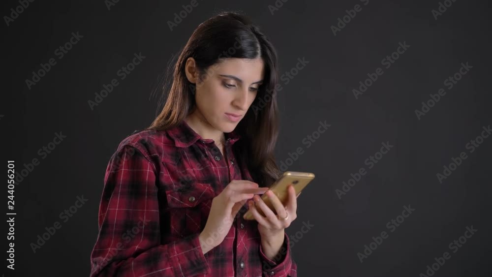 Portrait of young and beautiful caucasian long-haired girl attentively watching into smartphone on black background. Portrait of young and beautiful caucasian long-haired girl attentively watching into smartphone on black background.